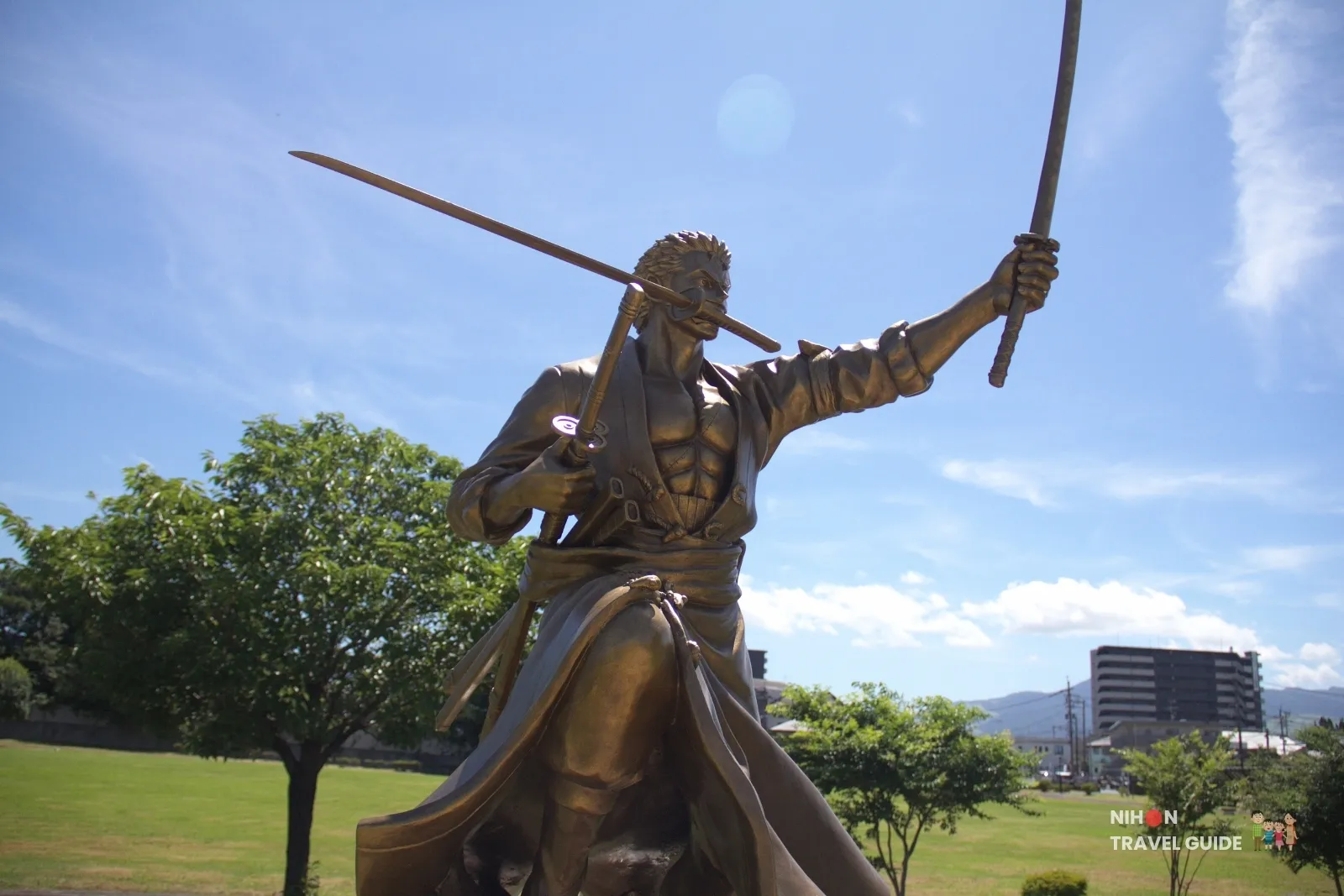 Low-angle close-up of the bronze Roronoa Zoro statue from One Piece holding three swords at Ozu Central Park in Kumamoto.