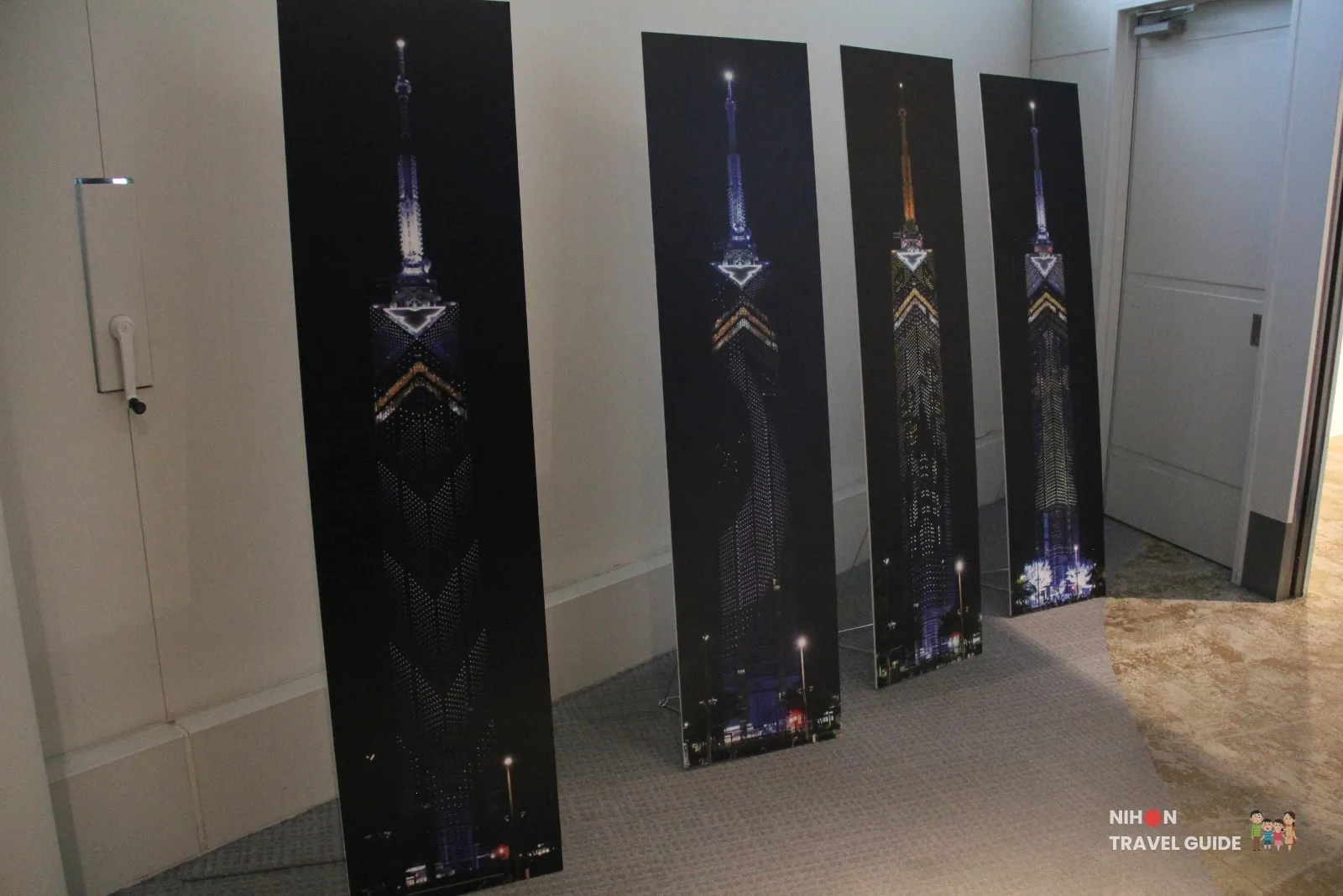 Four tall indoor banners showing Fukuoka Tower night illuminations in gold, blue, and purple light patterns.