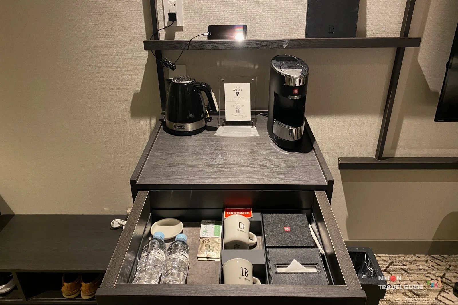Entry wall in a THE BASICS FUKUOKA Moderate Twin with wooden hangers, shoe shelf, in-room safe, minibar fridge, electric kettle, and illy coffee maker on a dark wood console.